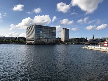 Modern buildings by river against sky in city