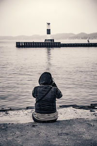 Rear view of person photographing lake while sitting on pier