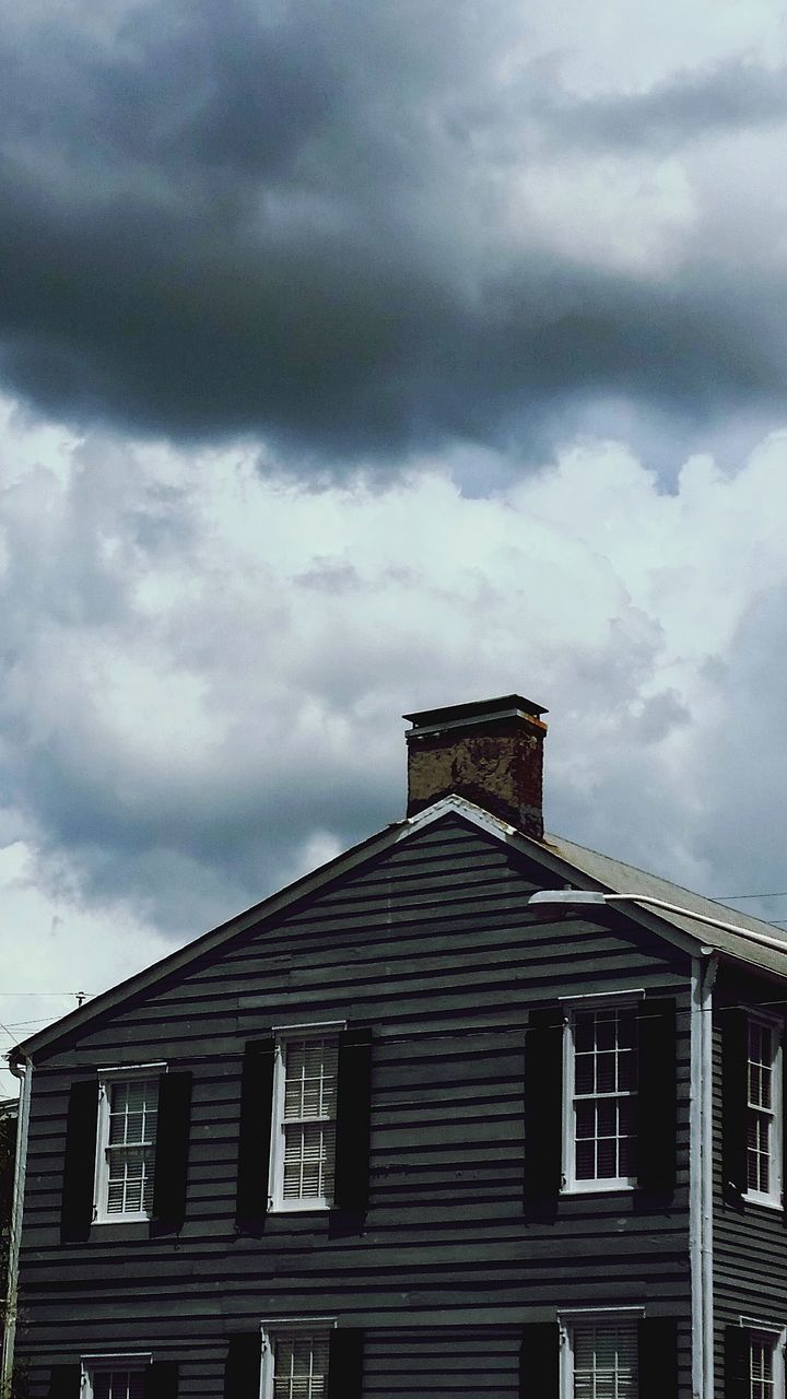 LOW ANGLE VIEW OF HOUSE ROOF AGAINST STORM CLOUDS