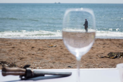 Drinking glass on beach against sea