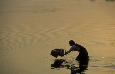 Side view of woman filling water in buckets while standing in sea