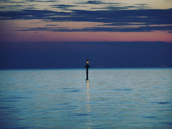 Low section of man fishing in sea against sky during sunset