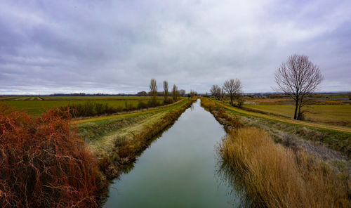 Panoramic shot of canal amidst field against sky