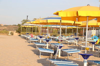 Empty chairs and tables at beach against sky