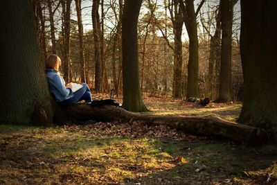 Man sitting by tree trunk in forest