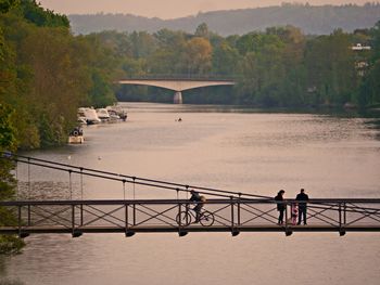 People standing on bridge over river against trees