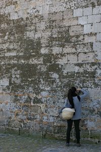 Rear view of woman photographing against wall