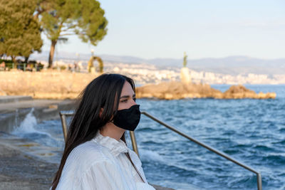 Young woman wearing black mask on sea shore. summer, tourism, virus, corona, covid-19.