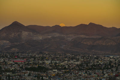 Aerial view of townscape by mountains against sky during moonrise