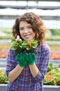 Portrait of smiling woman holding potted plants in greenhouse