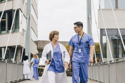 Male healthcare worker talking with female physician while walking on bridge