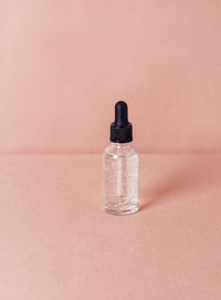 Glass bottle with liquid with bubbles on a shiny pink fabric background. serum or essential aroma 