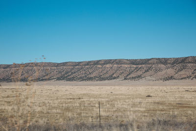 Scenic view of arid landscape against clear blue sky during sunny day