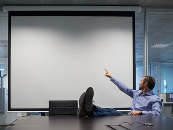 Businessman pointing towards projection screen while sitting in board room at office