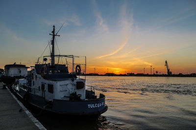 Ship moored at harbor against sky during sunset