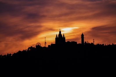 Low angle view of silhouette buildings against cloudy sky during sunset