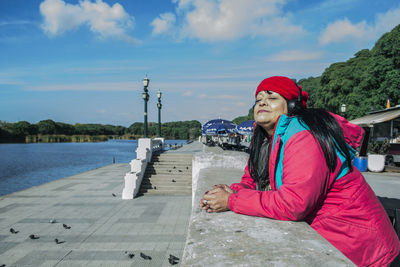 Woman listening music with headphones while standing at promenade by sea