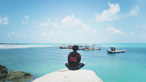 Rear view of man sitting on sea against sky