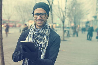 Portrait of man wearing warm clothing while using digital tablet in city