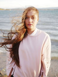 Portrait of beautiful young woman with tousled hair standing at beach