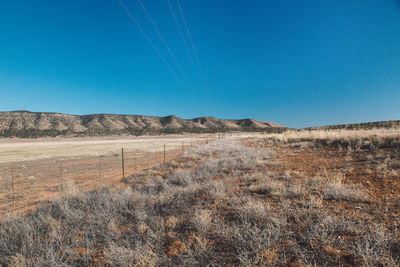 Scenic view of arid landscape against clear blue sky during sunny day