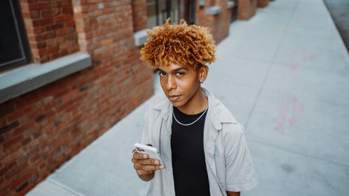 A young man is standing on a sidewalk looking at his cell phone