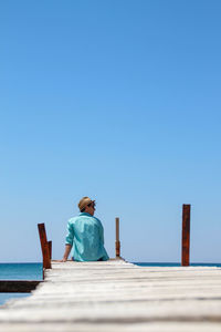 Boy dressed in a turquoise shirt sitting on an antique wooden catwalk over the mediterranean sea