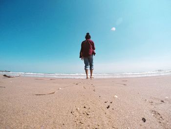 Rear view of man standing on beach against clear blue sky