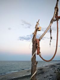 Rope on wooden post at beach against sky during sunset