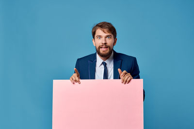 Portrait of businessman holding board against blue background