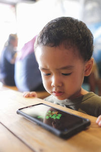 Close-up of boy looking through mobile phone on table