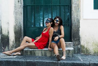 Portrait of two seated women wearing mask against green door.