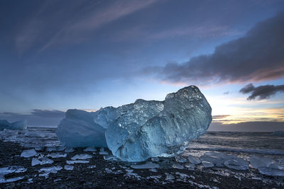 Iceberg at beach against sky during sunset