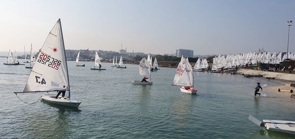People on sailboats in sea against sky