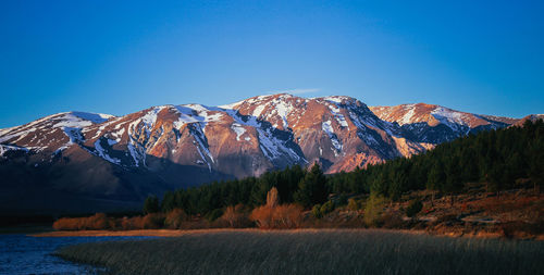 Calm countryside lake in front of mountains against clear blue sky