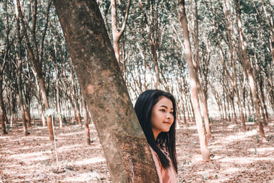 Portrait of woman standing by tree trunk in forest
