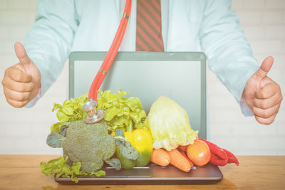 Midsection of man showing thumbs up sign by laptop and vegetables