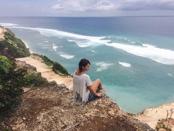 High angle view of young woman sitting on cliff by sea