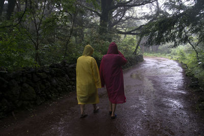 Rear view of friends wearing raincoat walking at bijarim forest during rainy season