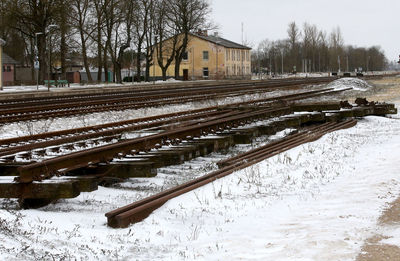 Snow covered railroad tracks by trees on field during winter