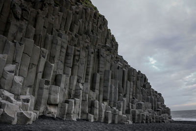 Stone structure on beach against cloudy sky