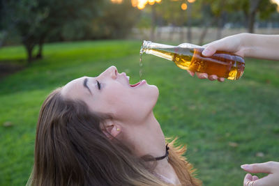 Cropped hand of friend pouring beer to woman at park