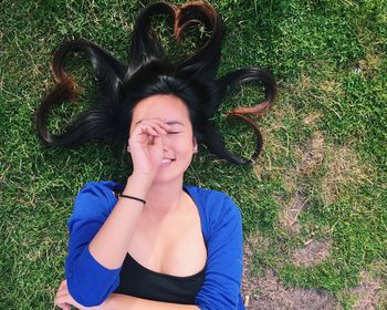 Young woman with heart shape made of hair lying on grassy field
