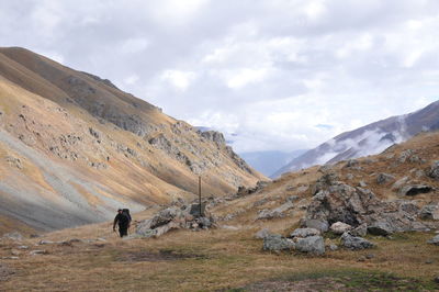 Hiker climbing mountain against cloudy sky