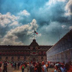 Group of people in front of building against cloudy sky