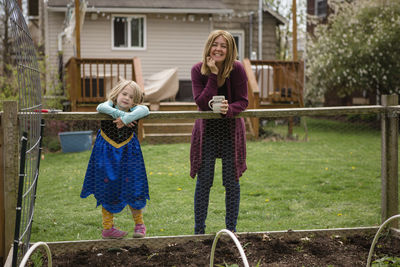 A mother and little girl in princess dress stand at edge of garden