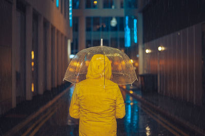 Rear view of woman with umbrella standing in city at night