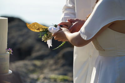 Midsection of couple cutting wedding cake against sky