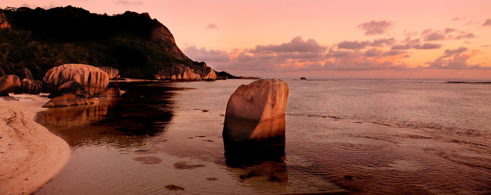 Rock formation on beach against sky during sunset