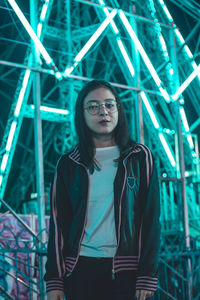 Portrait of smiling young woman standing against illuminated lights at night